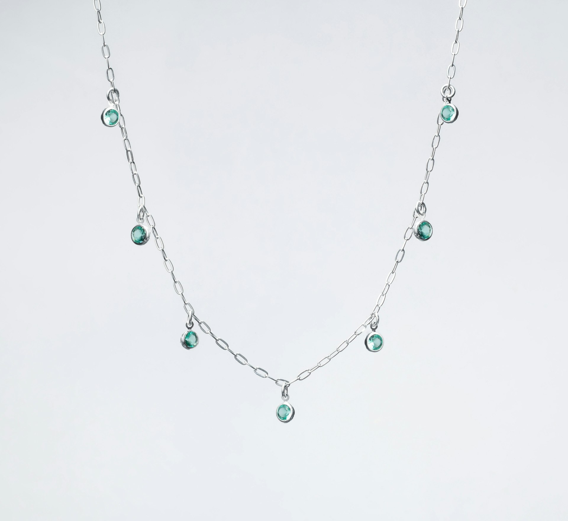 a silver necklace with green beads on a white background